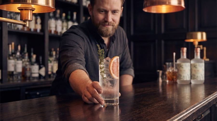 Bartender serviert einen Nord Gin & Tonic mit Thymian und Grapefruit an einer dunklen Bar
